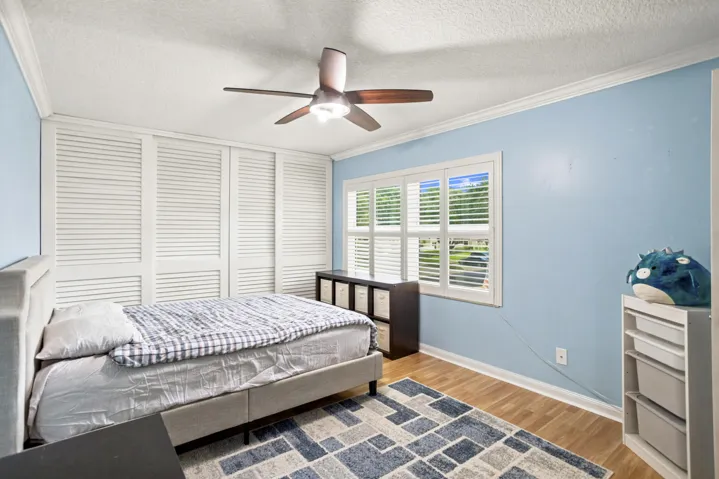 Wood-finish flooring, white window shutters, white crown molding, and a ceiling fan with light fixture