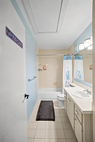 White vanity with integrated sink, overhead mirror with wall-mounted lighting, and a bathtub with shower