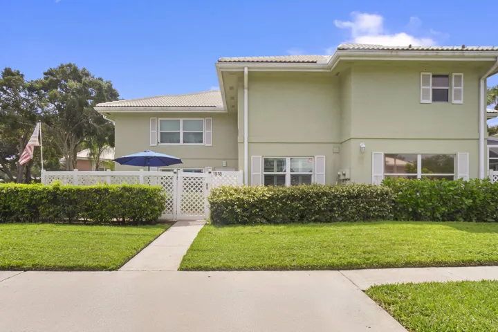 Stucco exterior with white shutters, white lattice fencing, and mature landscaping