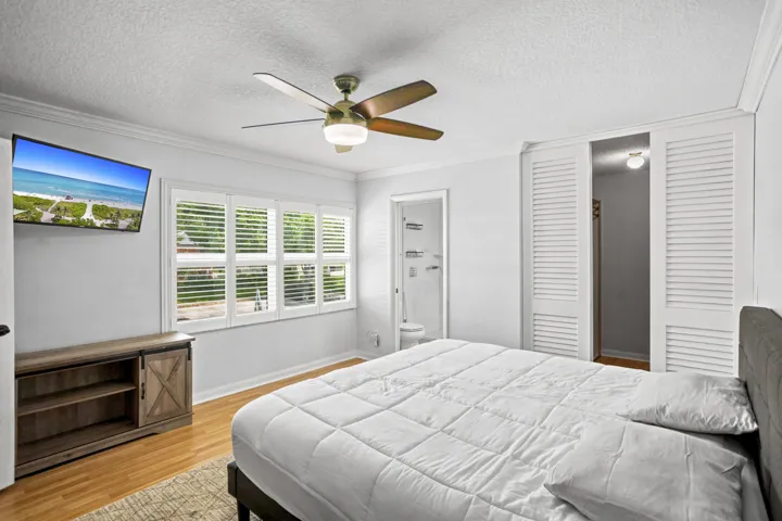 Wood-finish flooring, ceiling fan with integrated lighting, white louvered bifold doors, white plantation shutters, and crown molding