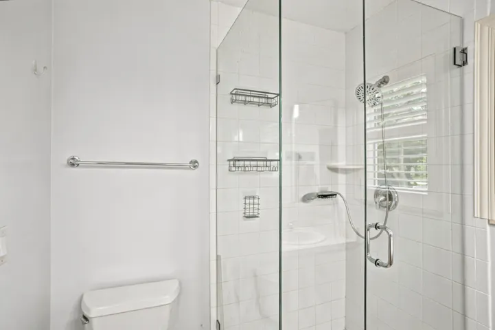 Glass-enclosed shower with white tiled walls, chrome fixtures, and a handheld showerhead
