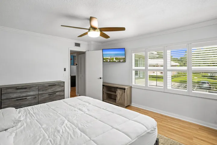 Crown molding detailing, hardwood-finish flooring, ceiling fan with integrated lighting, and multiple windows with plantation shutters