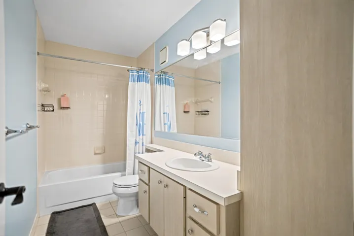 Bathroom featuring a single vanity with light-toned cabinetry, an integrated sink, a large wall mirror, and a full-size bathtub with a tiled surround