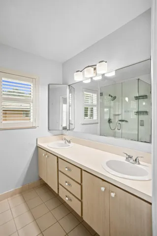Dual vanity with integrated sinks, expansive wall mirror, and a glass-enclosed shower