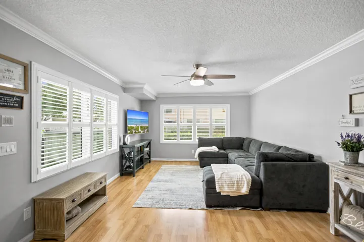 Light wood-finish flooring, white plantation shutters, crown molding, a ceiling fan with integrated lighting, and recessed ceiling details