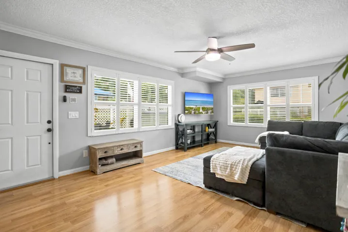 Wood-finish flooring, multiple windows with plantation shutters, ceiling fan with integrated lighting, and crown molding