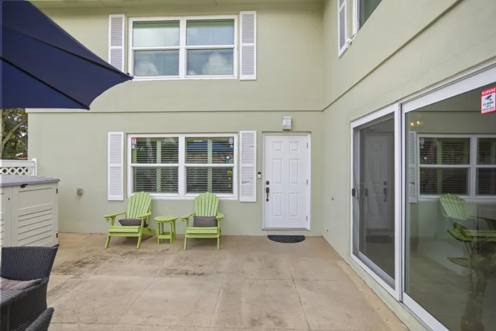 Two-story exterior with a stucco finish, multiple windows with white shutters, a white paneled door, and a sliding glass door