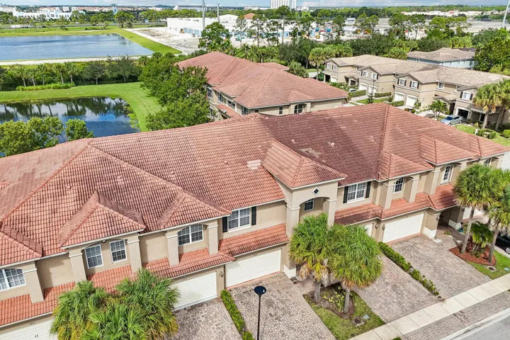 Townhome exterior featuring a red tile roof, stucco facade, multiple windows with dark shutters, and a paver driveway