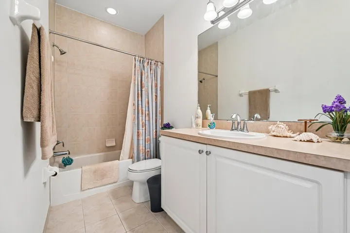 Light-toned tiled flooring, white vanity with integrated sink, chrome faucet, and a full-width mirror