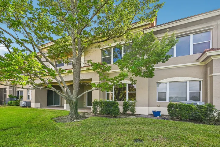Stucco exterior with multiple windows, mature tree, and a covered patio