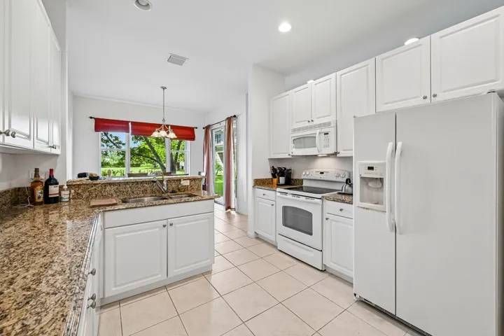 White cabinetry, granite-style countertops, stainless steel sink, built-in appliances, and tiled flooring