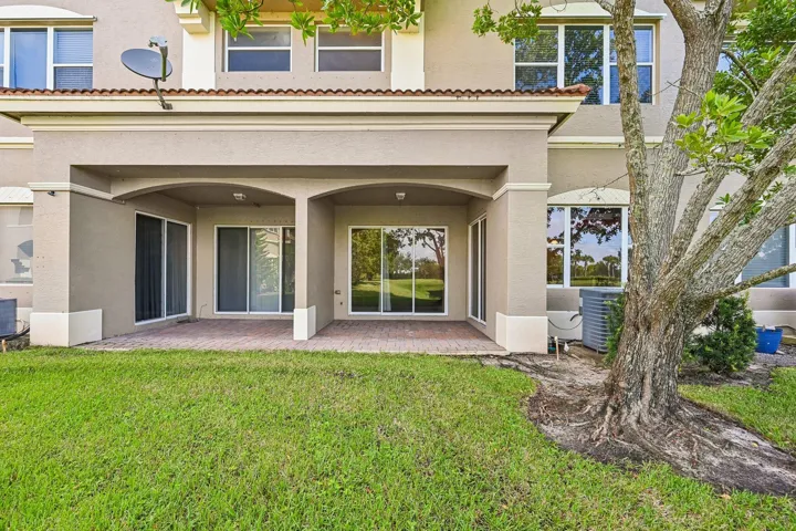 Covered patio with brick paver flooring, multiple sliding glass doors, and a manicured lawn