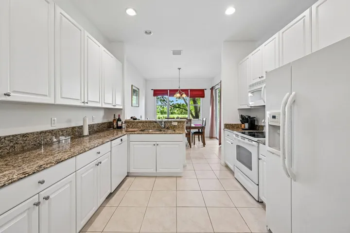 Spacious kitchen featuring white cabinetry, light-toned tile flooring, granite countertops, and recessed lighting