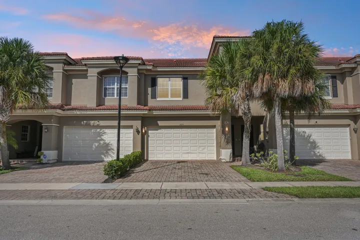 Stucco exterior with a tile roof, individual garage access, and paver driveways
