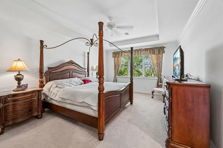 Tray ceiling, crown molding, white walls, carpet flooring, and a ceiling fan