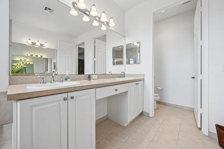 Dual vanity with integrated sinks, ample countertop space, white cabinetry, and large wall-mounted mirror