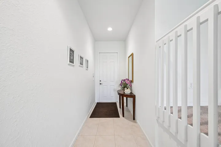 Recessed lighting illuminates the entryway, featuring tile flooring and a white paneled door