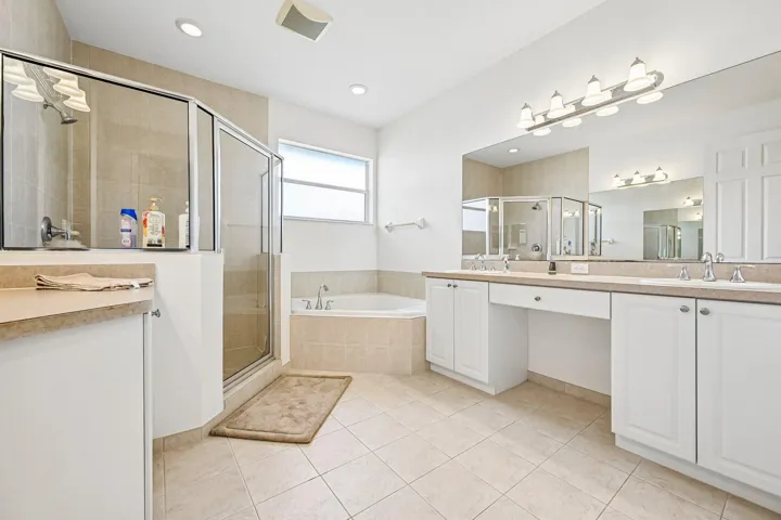 Spacious bathroom featuring a glass-enclosed shower, built-in corner tub, dual vanity with undermount sinks, white cabinetry, and light-toned tile flooring