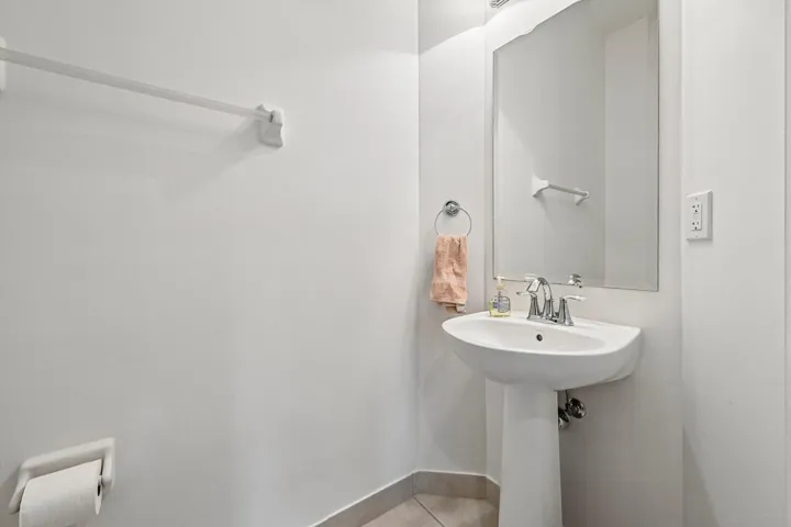 Pedestal sink with chrome faucet, wall-mounted mirror, and tile​​‌​​​​‌​​‌‌​‌‌​​​‌‌​‌​‌​‌​​​‌​​ flooring