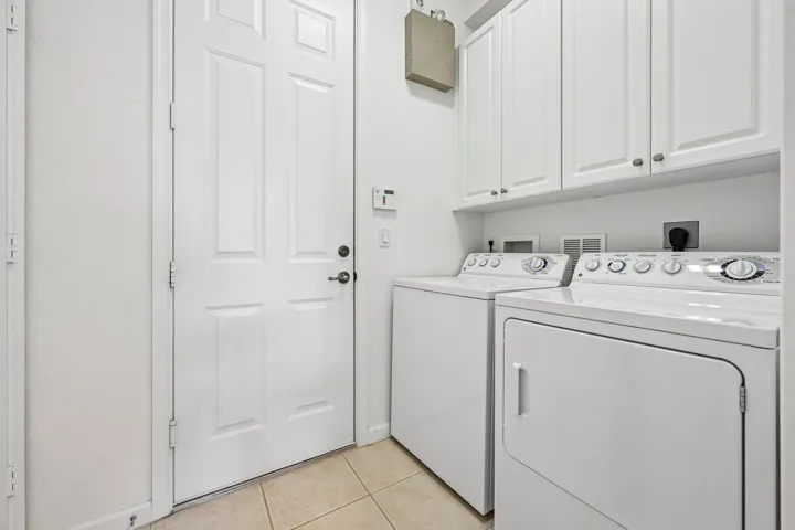 White cabinetry with chrome hardware, integrated washer and dryer, and neutral tile flooring