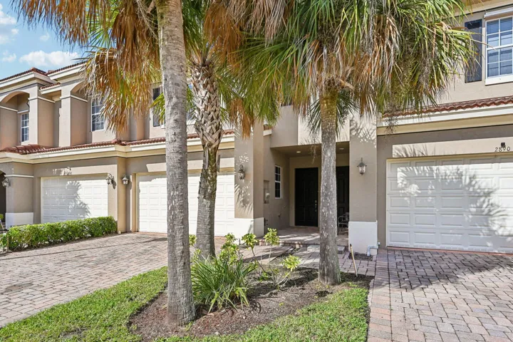 Multi-story stucco exterior with arched window details, a tile roof, brick paver driveway, and an integrated garage