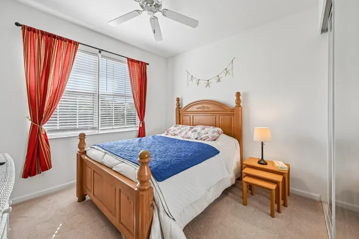 Wood-finish bed frame, carpeted flooring, window with blinds, ceiling fan, and mirrored closet doors