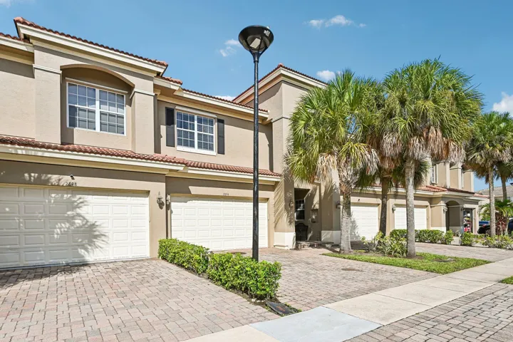 Stucco exterior with a tile roof, individual garage access, paver driveways, and mature palm trees