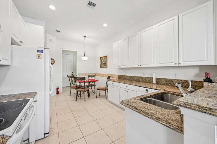White cabinetry with granite countertops, a dual basin sink, and tile flooring