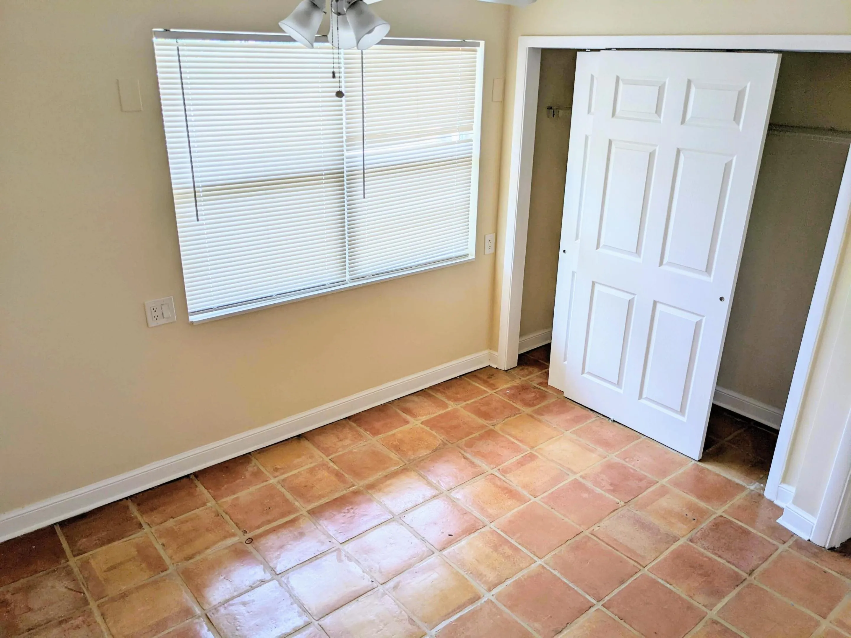Terracotta tile flooring, white bi-fold closet doors, white window blinds, and a ceiling fan with integrated lighting
