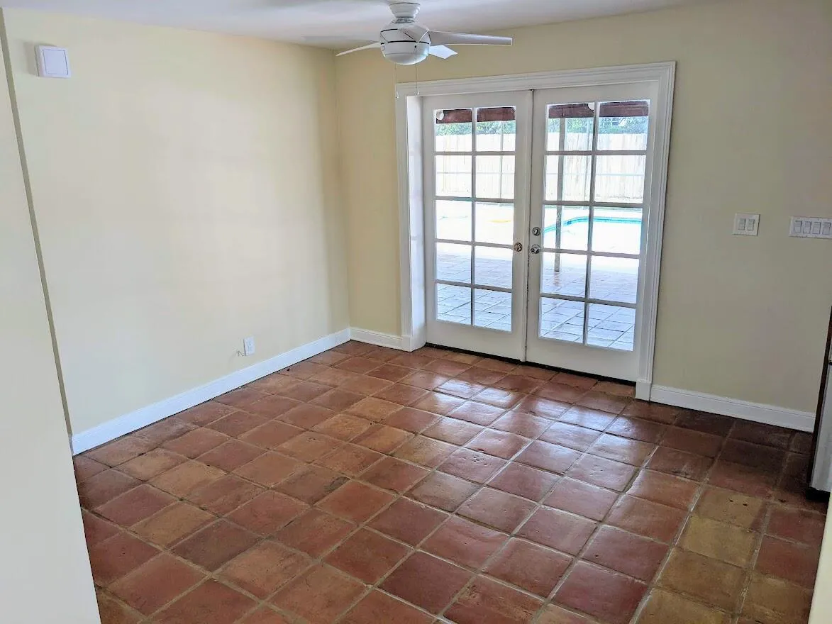 Terracotta tile flooring, white ceiling fan, and French doors leading to an outdoor patio with a visible swimming pool