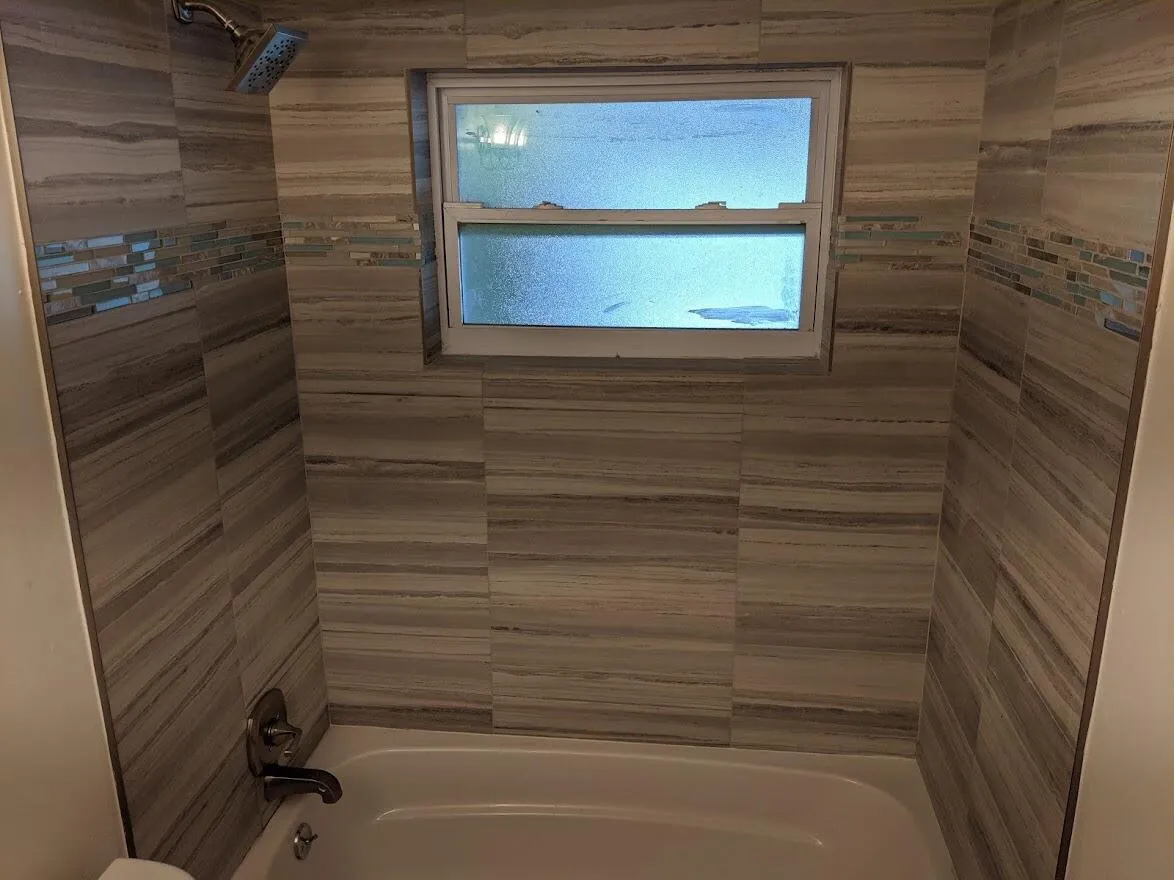 Bathtub with full-height tile surround, decorative tile accent band, and a window