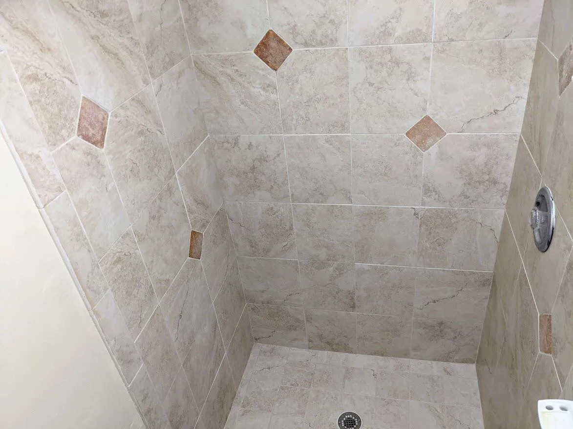 Tiled shower enclosure featuring light-toned large format tiles, accent diamond-shaped tiles, and a circular shower drain