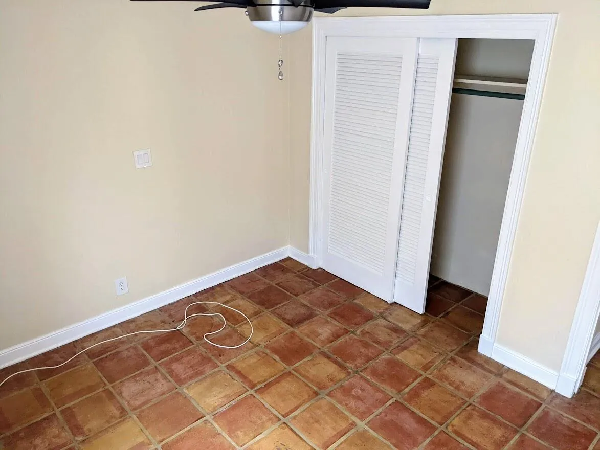 Terracotta tile flooring, white baseboards, and built-in closet with louvered bifold doors