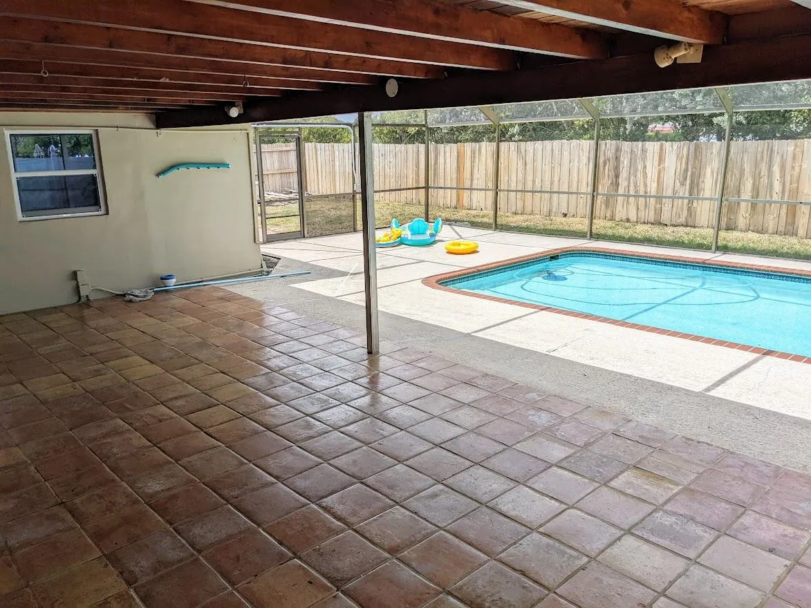 Covered patio with terracotta-style tile flooring, exposed wood beam ceiling, and screened-in swimming pool