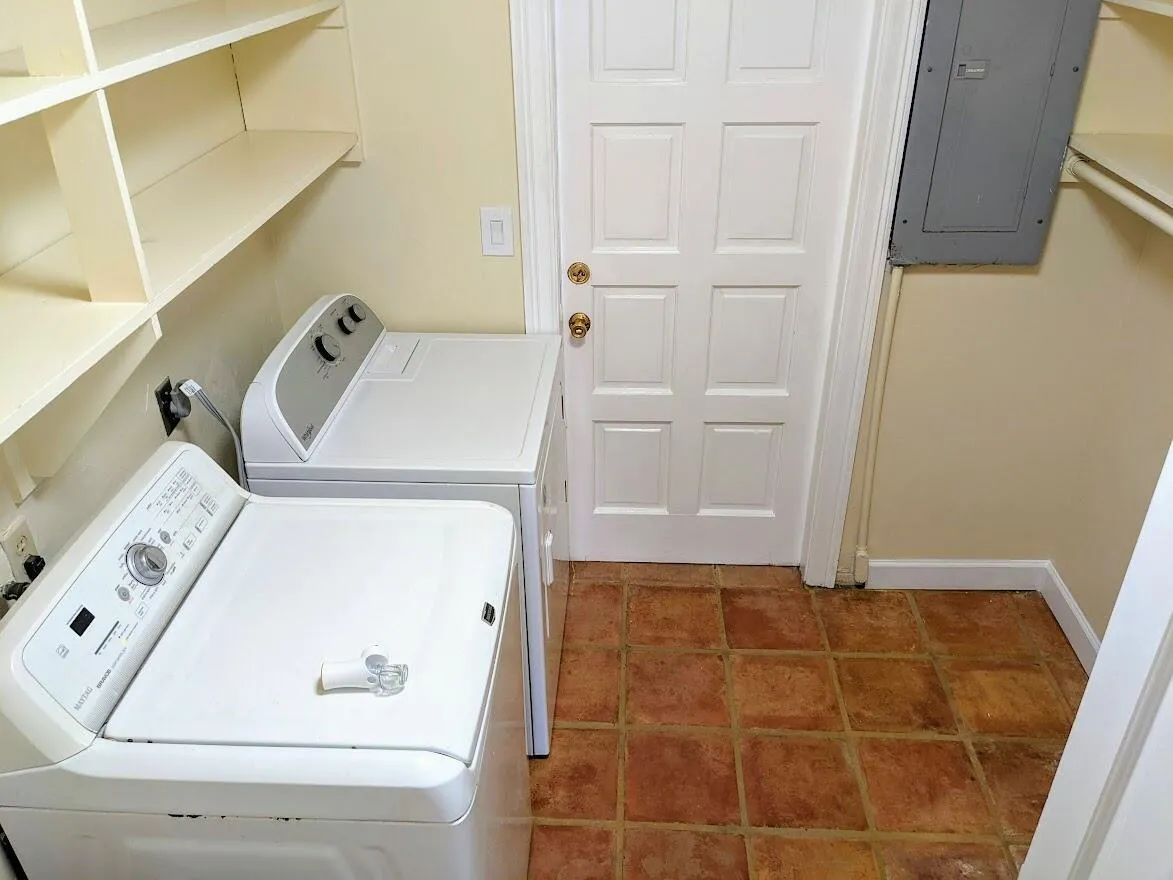 Utility area featuring terra cotta tile flooring, built-in shelving, and a paneled door