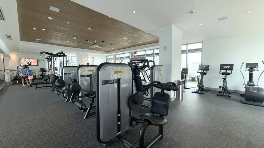 Fitness center featuring a recessed wood-paneled ceiling, large-format windows, rubberized flooring, and integrated ceiling fans
