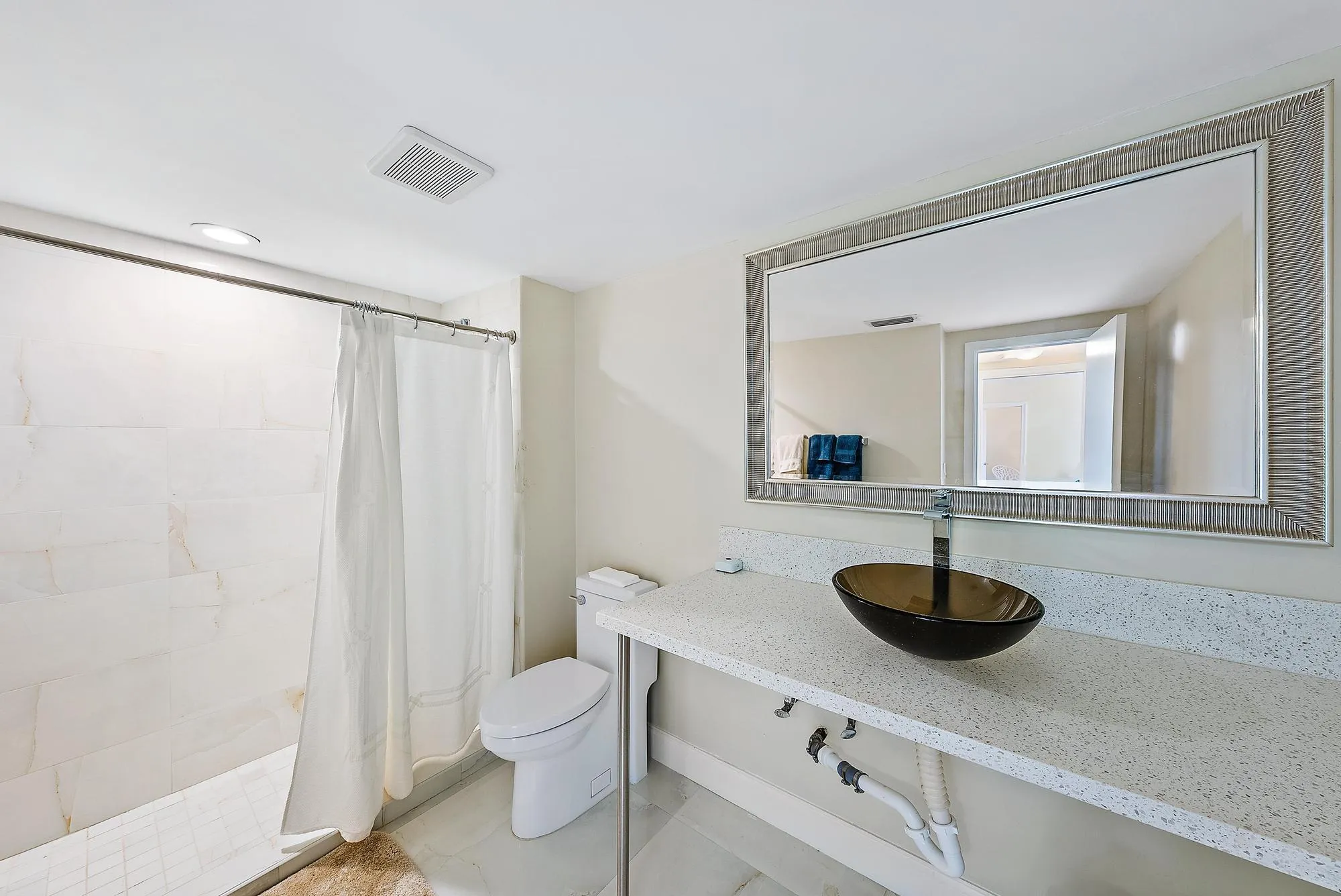 White tile flooring, full wall mirror, glass vessel sink, white countertop, and tiled shower surround