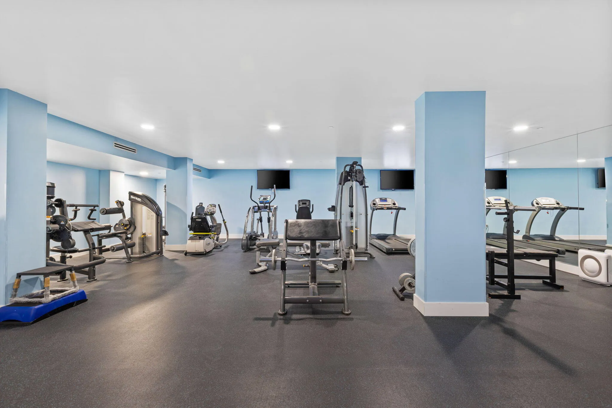 Fitness center featuring multiple exercise machines, mirrored wall, recessed lighting, and rubber flooring