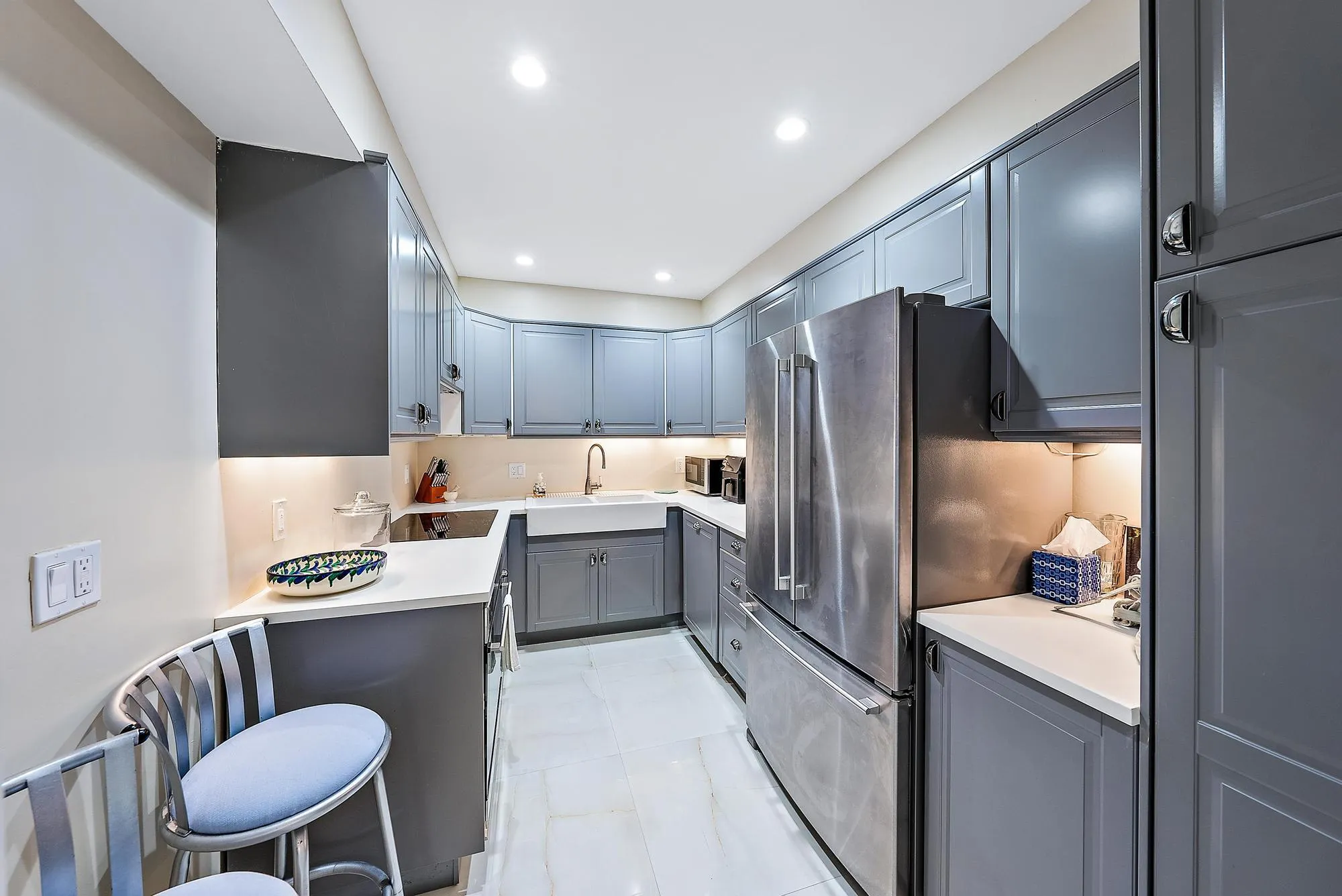 Galley kitchen featuring gray cabinetry, stainless steel appliances, a white farmhouse sink, and under-cabinet lighting