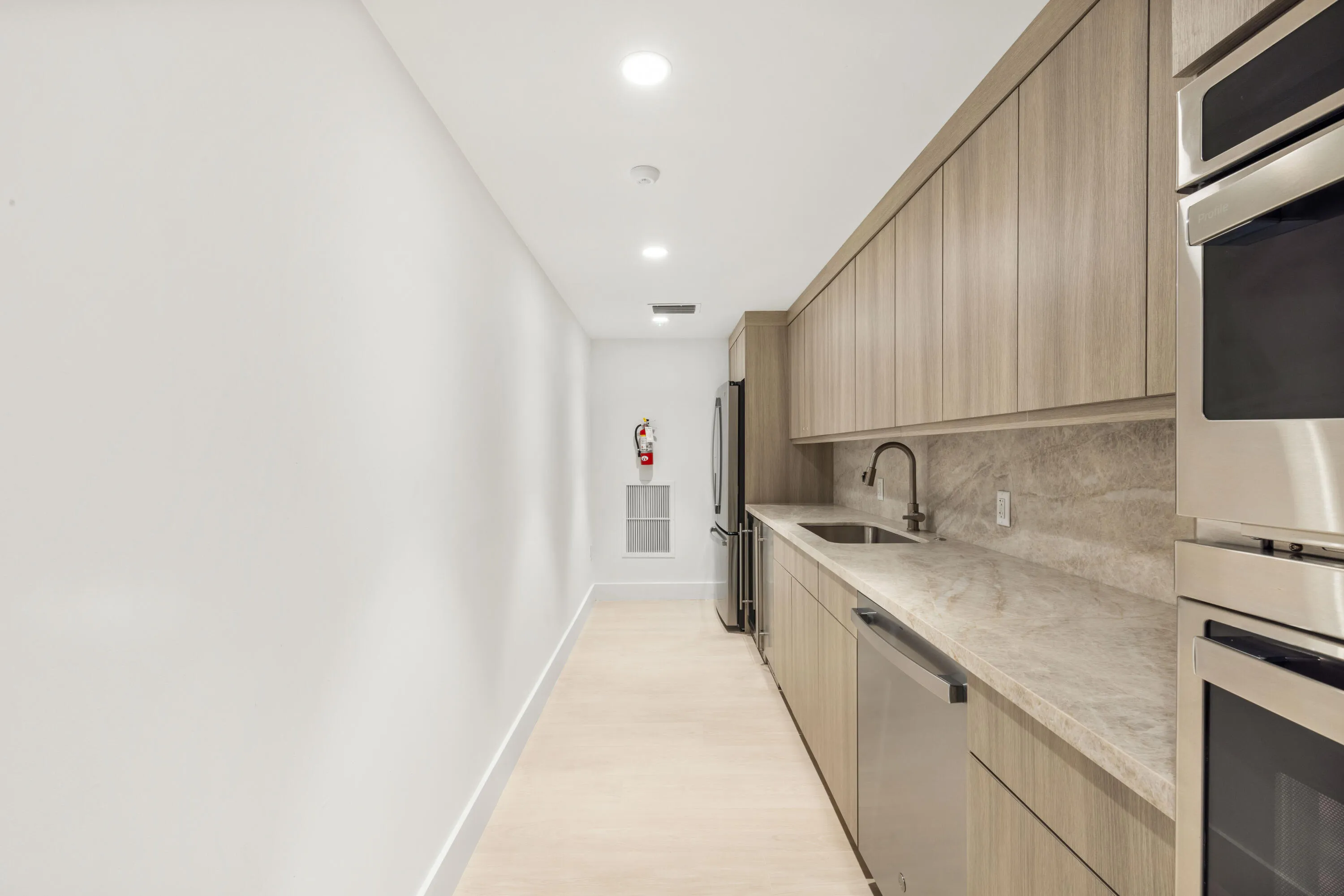 Integrated kitchen area featuring wood-finish cabinetry, stainless steel appliances, a matte black faucet, and stone countertops with a matching backsplash
