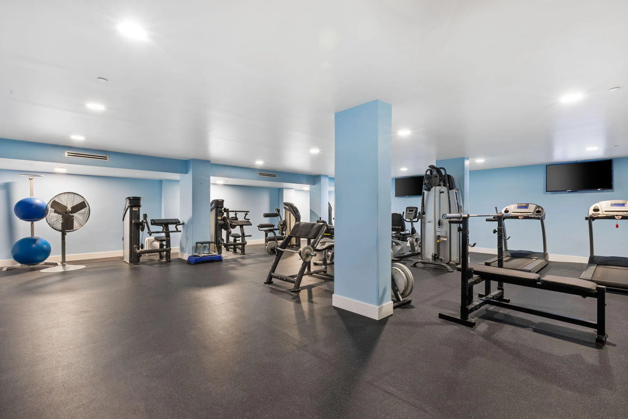 Fitness center with recessed lighting, light blue accent walls, and mounted television screens
