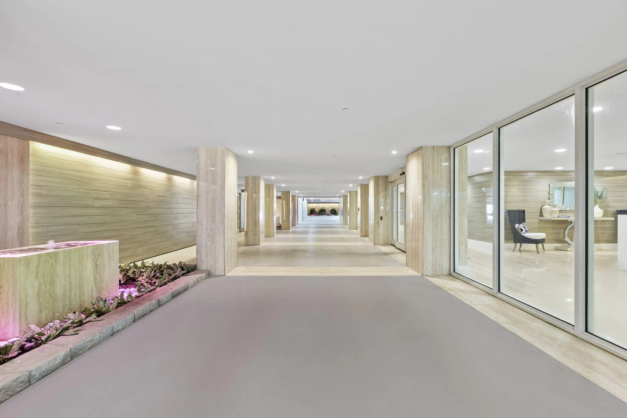 Recessed lighting illuminates a long hallway with full-height glass panels