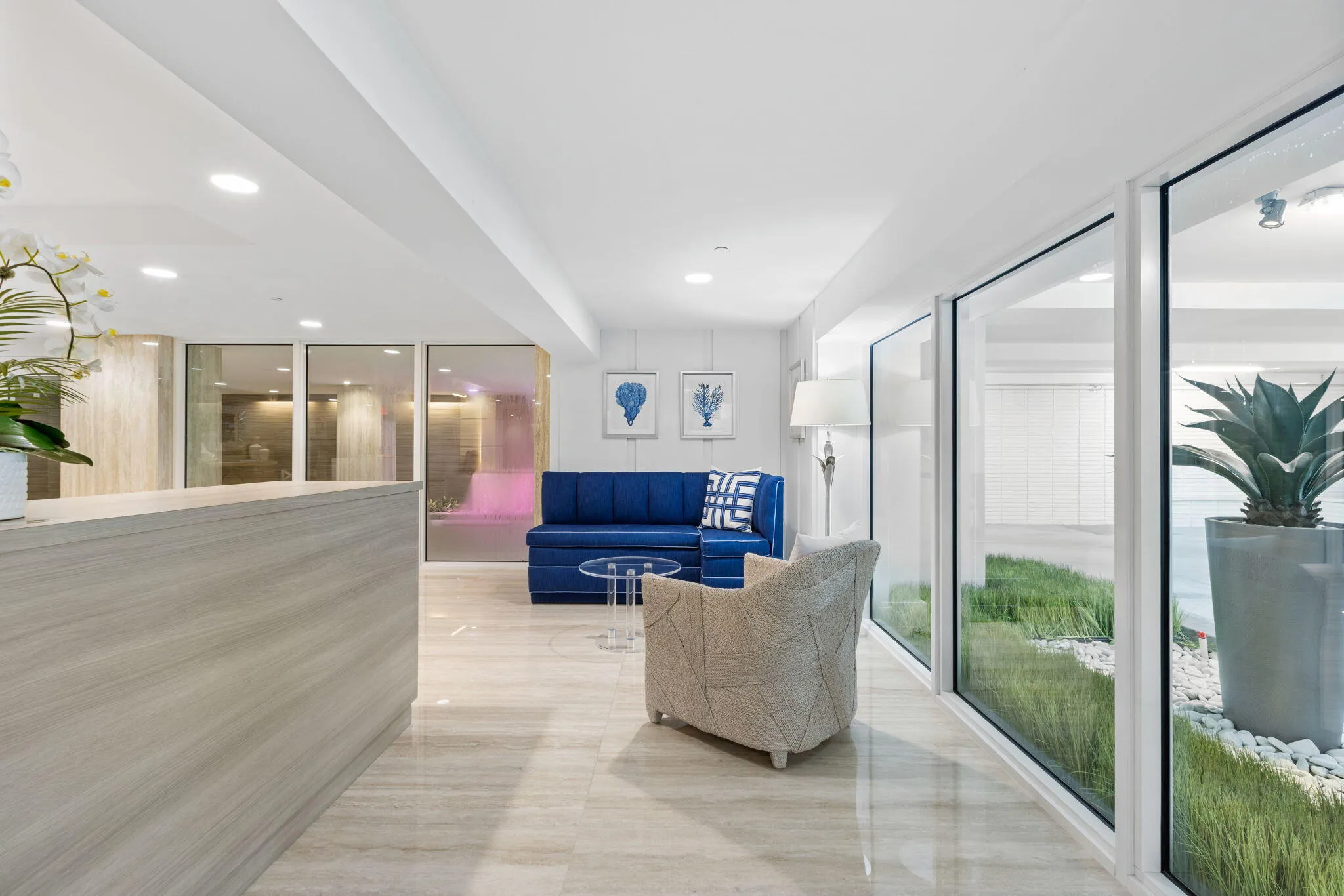 Light-toned tile flooring, recessed ceiling lighting, a reception desk with wood-finish paneling, and an interior planter with decorative white stones