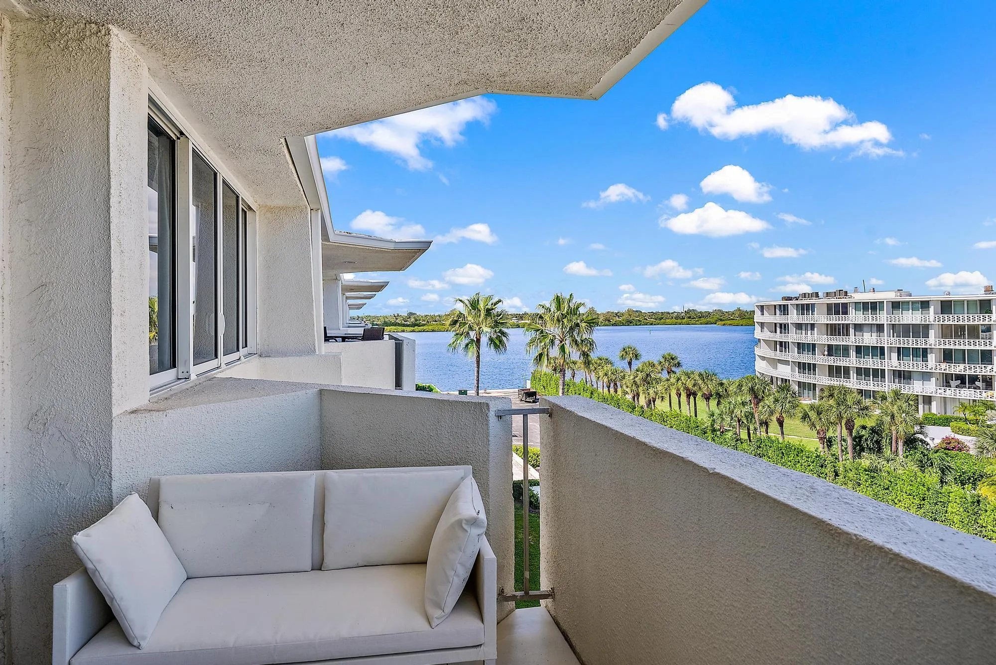 Balcony featuring a partial water body, palm trees, and distant building