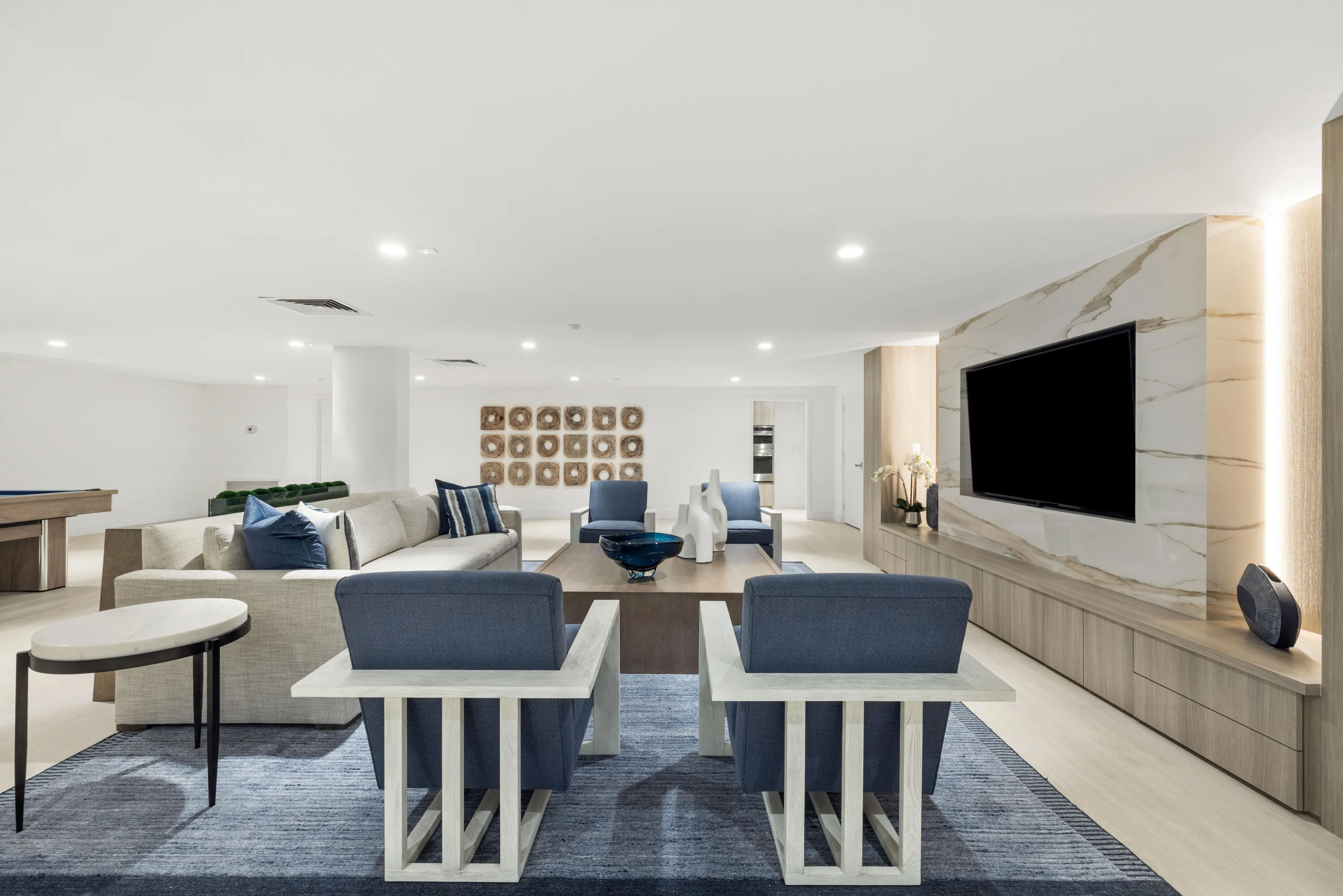 Recessed ceiling lighting, light wood-finish flooring, built-in entertainment unit with integrated lighting, a stone-finish accent wall, and a column-free open-concept layout