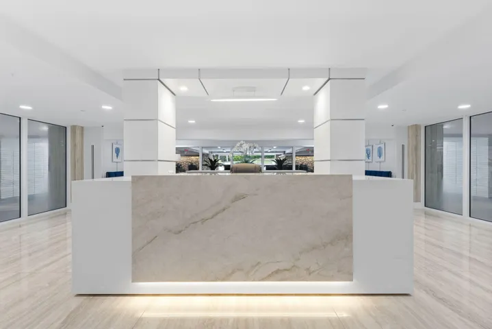 Lobby area featuring a stone-finish reception desk with integrated lighting, polished tile flooring, and recessed ceiling lighting