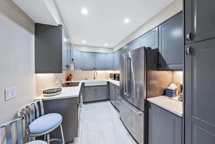 Galley kitchen featuring gray cabinetry, stainless steel appliances, a white farmhouse sink, and under-cabinet lighting
