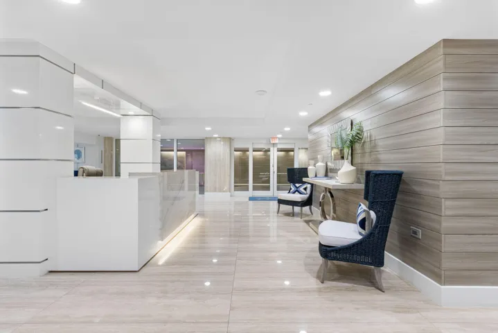 Polished stone flooring, wood-panel accent wall, recessed lighting, white reception desk with stone countertop, and contemporary seating