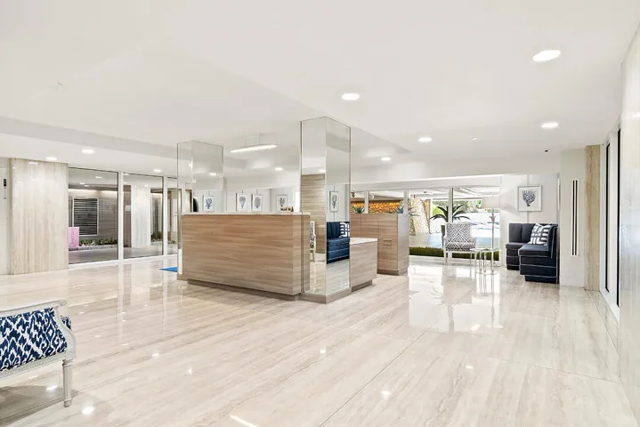 Polished stone tile flooring, recessed ceiling lighting, wood-finish reception desk, mirrored columns, and expansive glass exterior