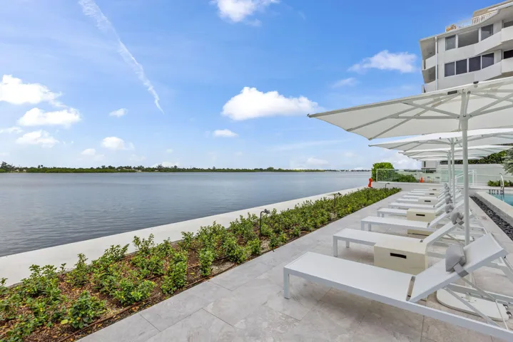 Waterfront property featuring a paver patio with landscaping, lounge chairs, and shade umbrellas
